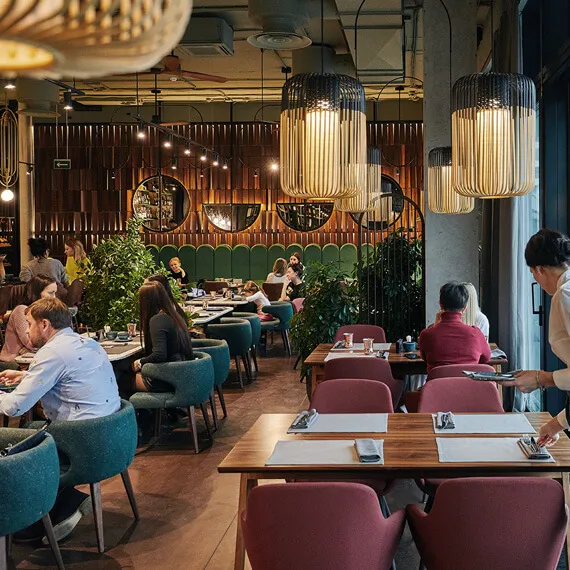 Warmly lit restaurant dining room with upholstered chairs and pendant lamps