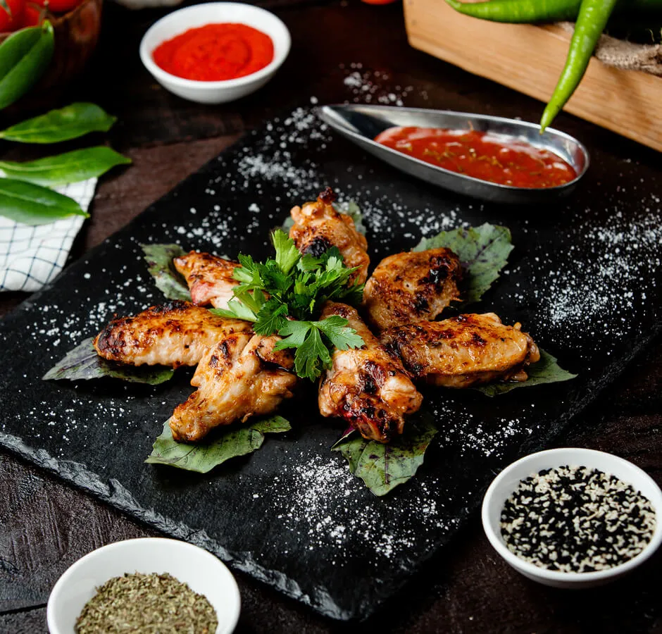 Golden glazed chicken on a dark plate with fresh herbs and dipping sauce